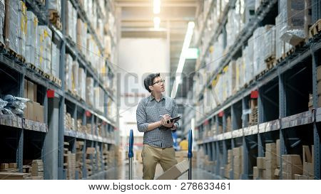 Young Asian Man Worker Doing Stocktaking Of Product In Cardboard Box On Shelves In Warehouse By Usin