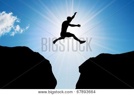 Man jumping over precipice between two rocky mountains at sun light. Freedom, risk, challenge, success.