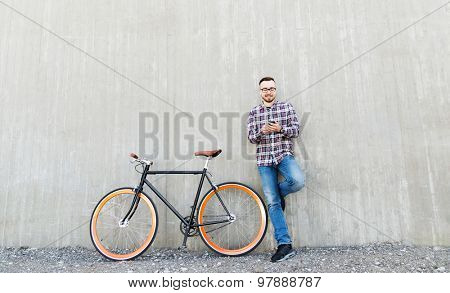 people, style, technology, leisure and lifestyle - happy young hipster man in earphones with smartphone and fixed gear bike listening to music on city street