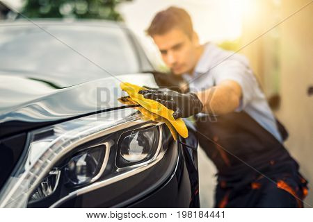 Car detailing - the man holds the microfiber in hand and polishes the car. Selective focus.