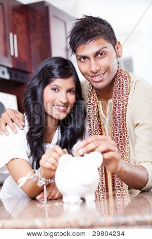 beautiful indian couple putting coins in piggybank