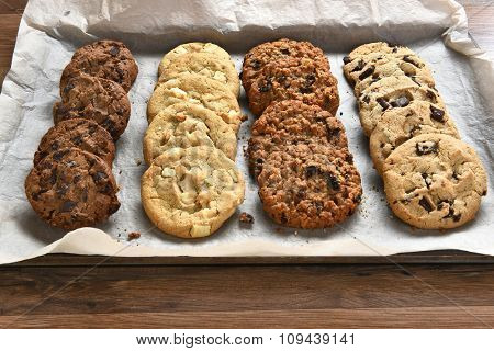 Closeup of a tray of fresh baked cookies, Chocolate Chip, oatmeal raisin Chocolate and white chocolate chip cookies on baking sheet and parchment paper.