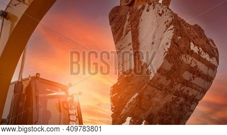 Backhoe Digging Soil At Construction Site. Dirt Bucket Of Backhoe Digging Soil With Yellow Sunset Sk