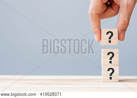 Hand Holding Questions Mark ( ? ) On Wooden Cube Block On Table Background. Faq( Frequency Asked Que