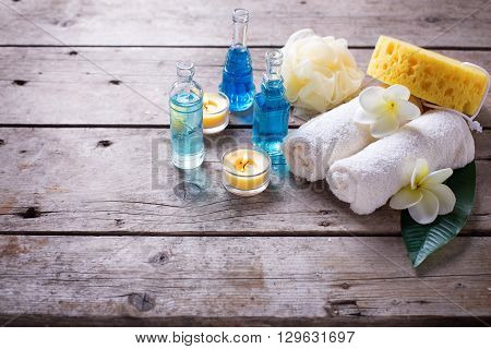 Spa or wellness setting in blue yellow and white colors. Bottles wih essential aroma oil towels candles and wispes on wooden background. Selective focus. Place for text.