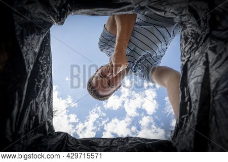 The Man Looks Into The Trash Can And Covers His Nose From The Strong Stench.