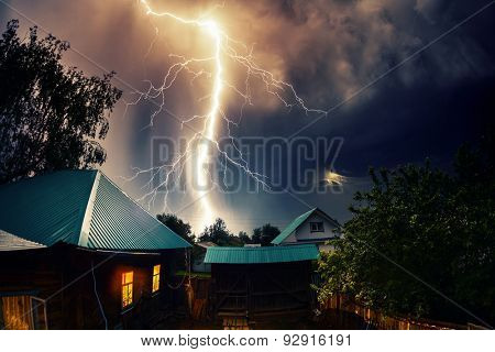 Thunderbolt over the house with dark stormy sky on the background and moon shining through the cloud