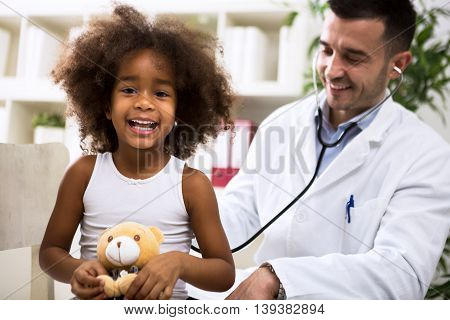 Pediatrician doctor examining happy smiling kid at hospital