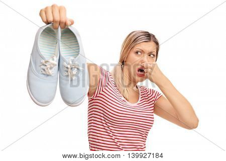 Disgusted woman holding a pair of stinky shoes isolated on white background