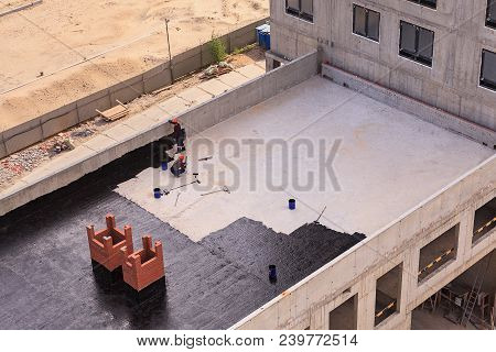 Two Workers Conduct Waterproofing Of The Roof With Bitumen. View From Above.