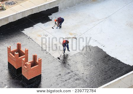 Two Workers Conduct Waterproofing Of The Roof With Bitumen. View From Above.