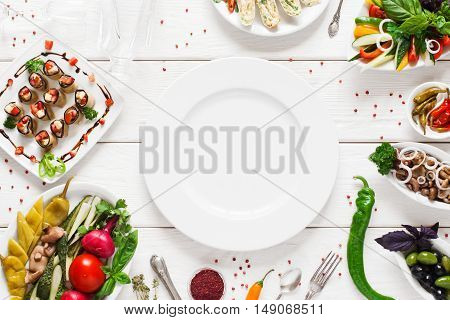 White ceramic plate surrounded by snacks, void. Variety of vegetarian meals make frame for empty dish. Cuisine, menu, food concept