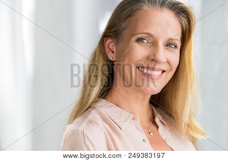 Portrait of mature woman enjoying life after retirement and looking at camera. Closeup face of happy senior woman with blond hair smiling. Beautiful smiling lady indoor.