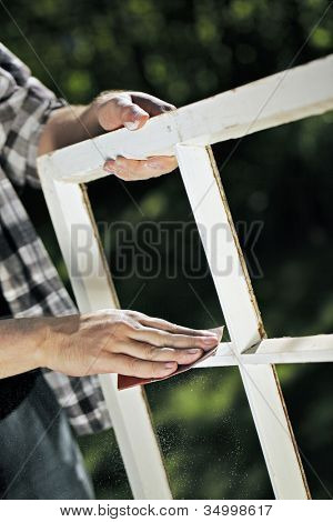 Man using a piece of abrasive sandpaper on an old window frame.