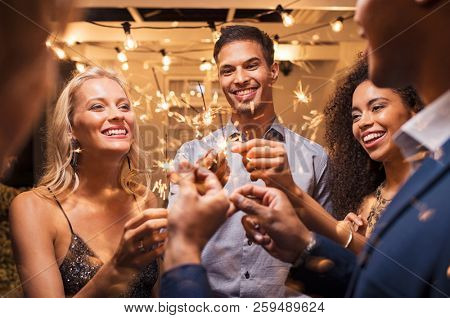 Group of multiethnic friends having fun with sparkling sticks during night party. Group of elegant women and men holding sparklers and celebrating the new yearâs eve.