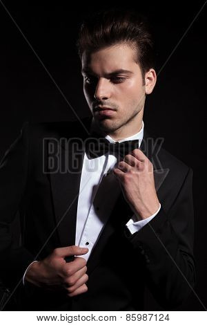 Young business man looking down while fixing his jacket and bowtie.