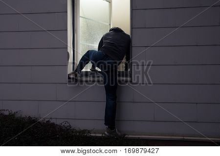 Rear View Of A Burglar Entering In A House Through A Window