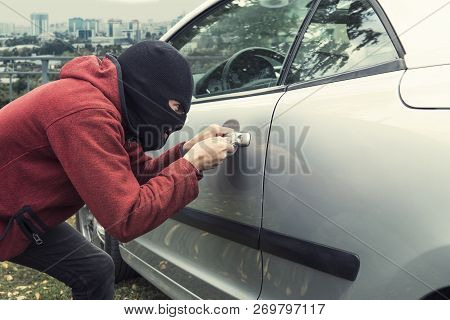 Close Up Of Man In Black Robber Mask Breaking The Car Lock On A City Background. Ill-intended Thief 