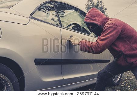 Side View Of Car Being Forced By A Man In Hoodie And Mask. Thief Tries To Steal Vehicle From A Parki