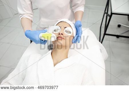 Woman Lies At Reception In Cosmetology Clinic And Does Facial Cleansing Using Laser And Modern Equip