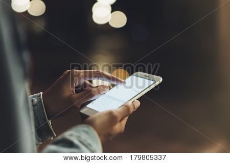 Girl pointing finger on screen smartphone on background illumination bokeh color light in night atmospheric city hipster using in female hands and texting mobile phone mockup glitter street content lifestyle