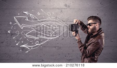 A hipster guy opening his point of view through looking a vintage camera concept with illustratied drawn arrows on urban wall