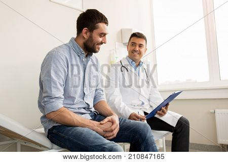 medicine, healthcare and people concept - smiling doctor with clipboard and young man patient meeting at hospital