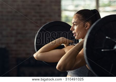 Fitness woman doing shoulder press exercise with a weight bar at gym. Muscular woman in gym doing heavy weight exercises. Concentrated athlete doing barbell lifting at health club with copy space.