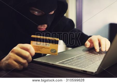 Man In Robber Mask And Hood Misappropriates Personal Bank Data. Cyber Fraudster Attacks Online Banki