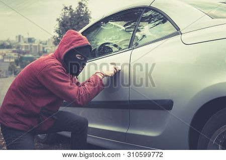 Masked Man In Casual Wear Furtively Picks The Car Lock On A City Background. Male Thief Stealthily P