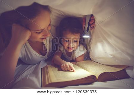 Family Reading Bedtime. Mom And Child Reading Book With A Flashlight Under Blanket