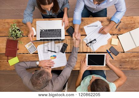 High angle view of businesspeople shaking hands and closing a deal. Successful business teamwork working at the office. Business partners sitting at table and planning work. 