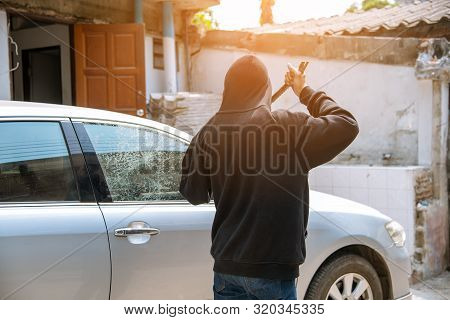 Car Thief Stealing To Break Glass Into A Car .masked Hide Face Man ,robber Dressed In Black Holding 