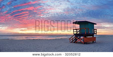 Miami South Beach sunrise with lifeguard tower and coastline with colorful cloud and blue sky.