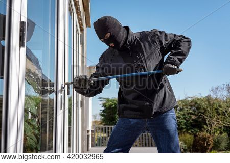 Burglar or thief breaking into a home through window with a crowbar