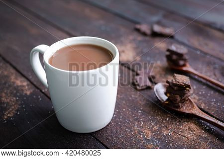 Chocolate Milk In White Cup With Bar Chocolate In Spoon On Wooden Table Background. Coco Hot Drink I