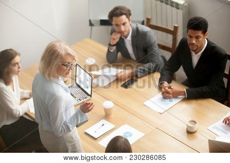 Serious Mature Woman Team Leader Speaking To Diverse Young People At Meeting, Senior Female Executiv