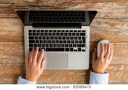 business, education, people and technology concept - close up of female hands with laptop and computer mouse on table