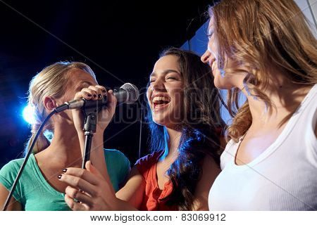 party, holidays, celebration, nightlife and people concept - happy young women singing karaoke in night club