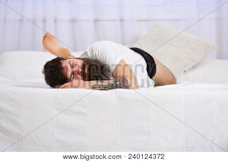 Guy On Calm Face Sleeping On Edge Of Bed On White Sheets. Man Laying On Bed, White Curtains On Backg