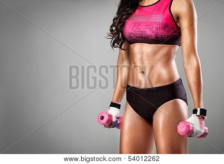 Torso of a young fit woman lifting dumbbells on a grey  background