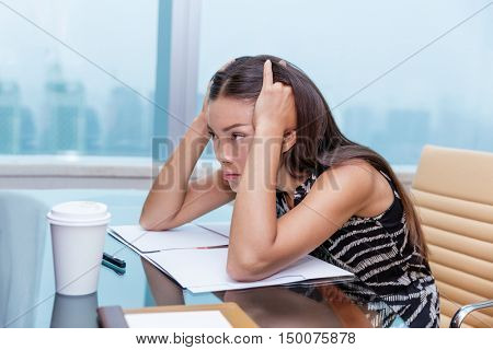 Stressed business woman at office desk stressing about work. Negative concept, headache, migraine. Tired businesswoman sitting thinking about problems and showing dissatisfaction of career.