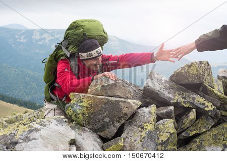 Helping hand - hiker man getting help on hike smiling happy overcoming obstacle. Hikers climbing on rock mountain at sunset one of them giving hand and helping to climb. Help support assistance in a dangerous situation. Concept teamwork.