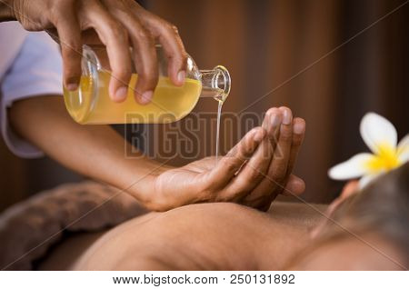 Closeup of masseur hands pouring aroma oil on woman back. Masseuse prepare to do oriental spa procedure for relaxing treatment. Therapist doing aromatherapy oil massage on woman body.