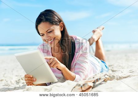 mulher despreocupada usa tecnologia de tablet touchpad na praia com as férias da internet