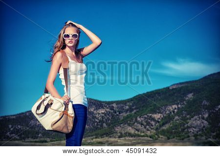 Beautiful young woman posing on a road over picturesque landscape.