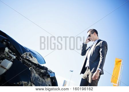 close-up of male adult man in suit, businessman, dealer checking damaged crashed black car after car accident, sunny daytime, winter