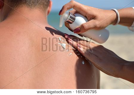 Hand Of A Woman Applying Sun Cream On A Male Back With Sunscreen Before Sunbathing At The Beach. Sun