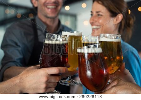 Happy friends clinking glasses of tap beer. Closeup hands of mature men and women toasting with draught beer. People holding beer for raising a toast to celebrate, cheering success with pints of beer.