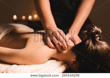 Men's Hands Make A Therapeutic Neck Massage For A Girl Lying On A Massage Couch In A Massage Spa Wit